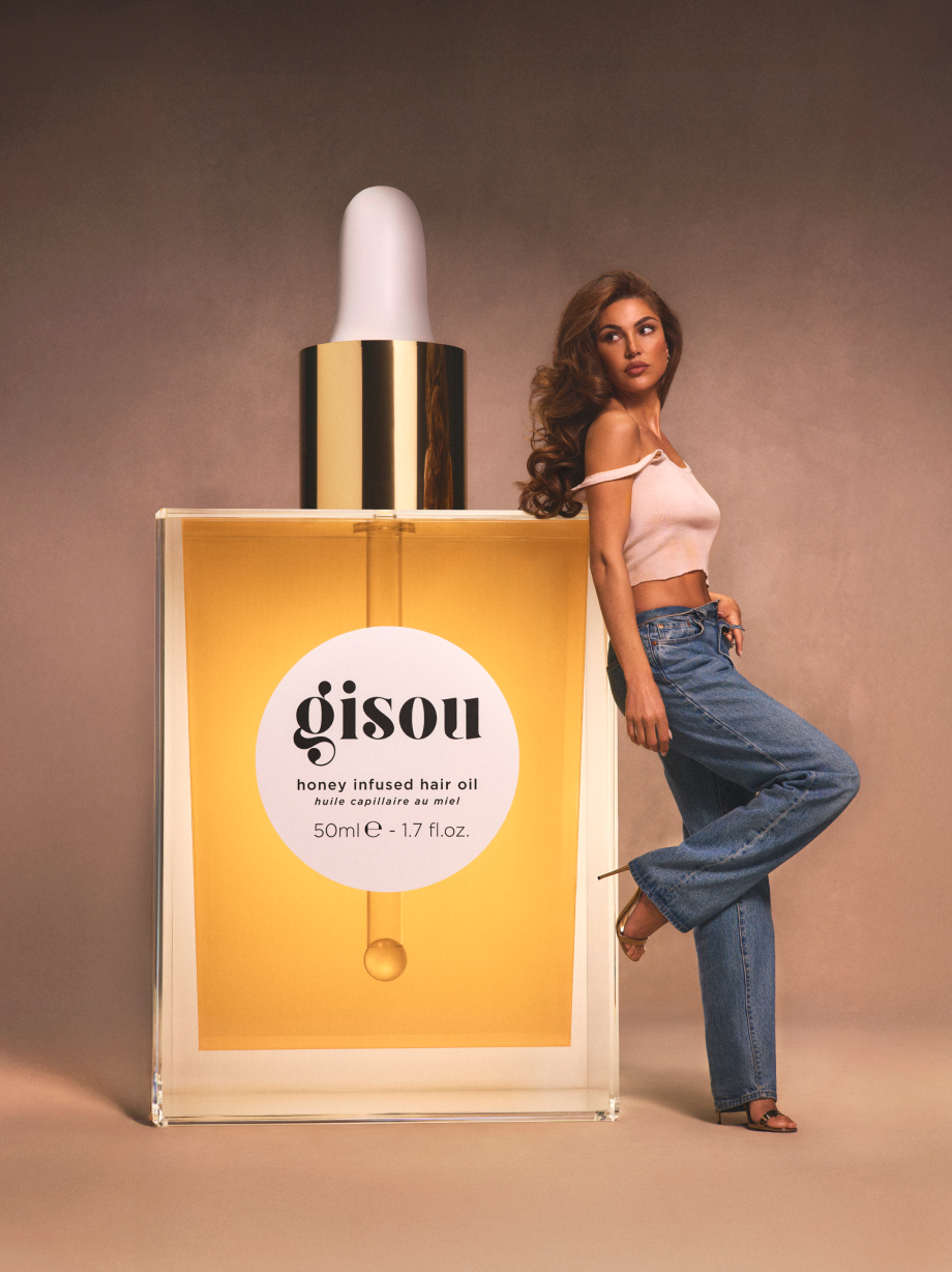 Negin Mirsalehi posing with a life-size Gisou Hair Oil.